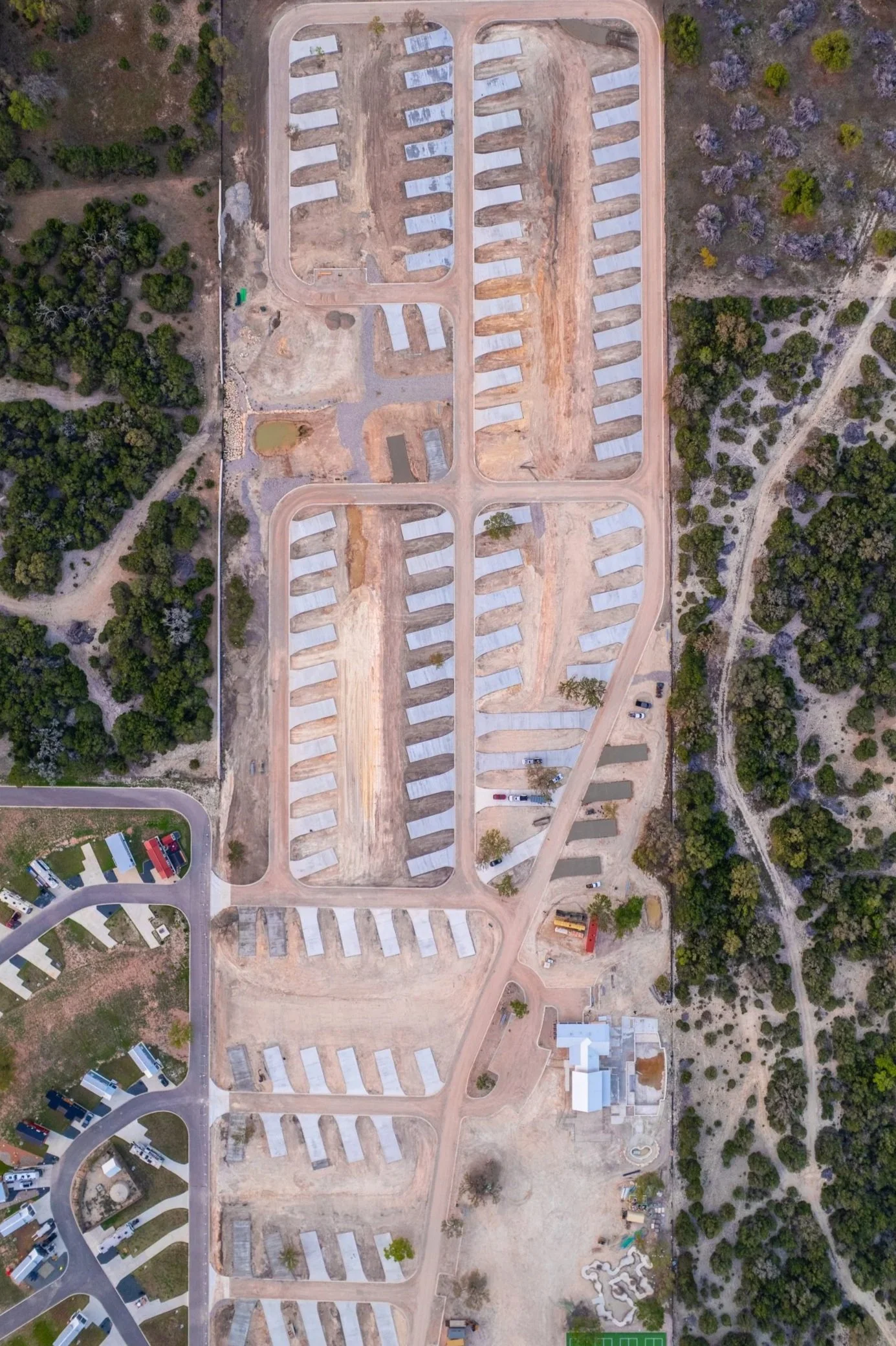 Aerial view of a construction site for a trailer park or RV park with gravel parking pads and roads surrounded by trees.