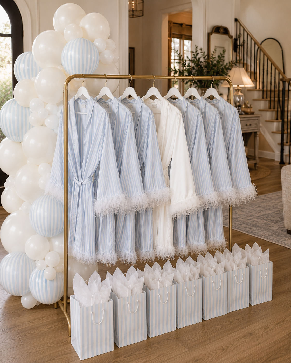 A clothing rack with blue and white striped robes and a white robe, surrounded by white balloons and gift bags in a decorated room.