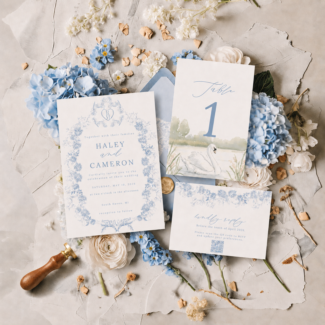 Wedding invitation suite with floral accents, including RSVP card, table number, and invitation card in blue and white with swan illustration surrounded by flowers, floral decorations, and a wax stamp.