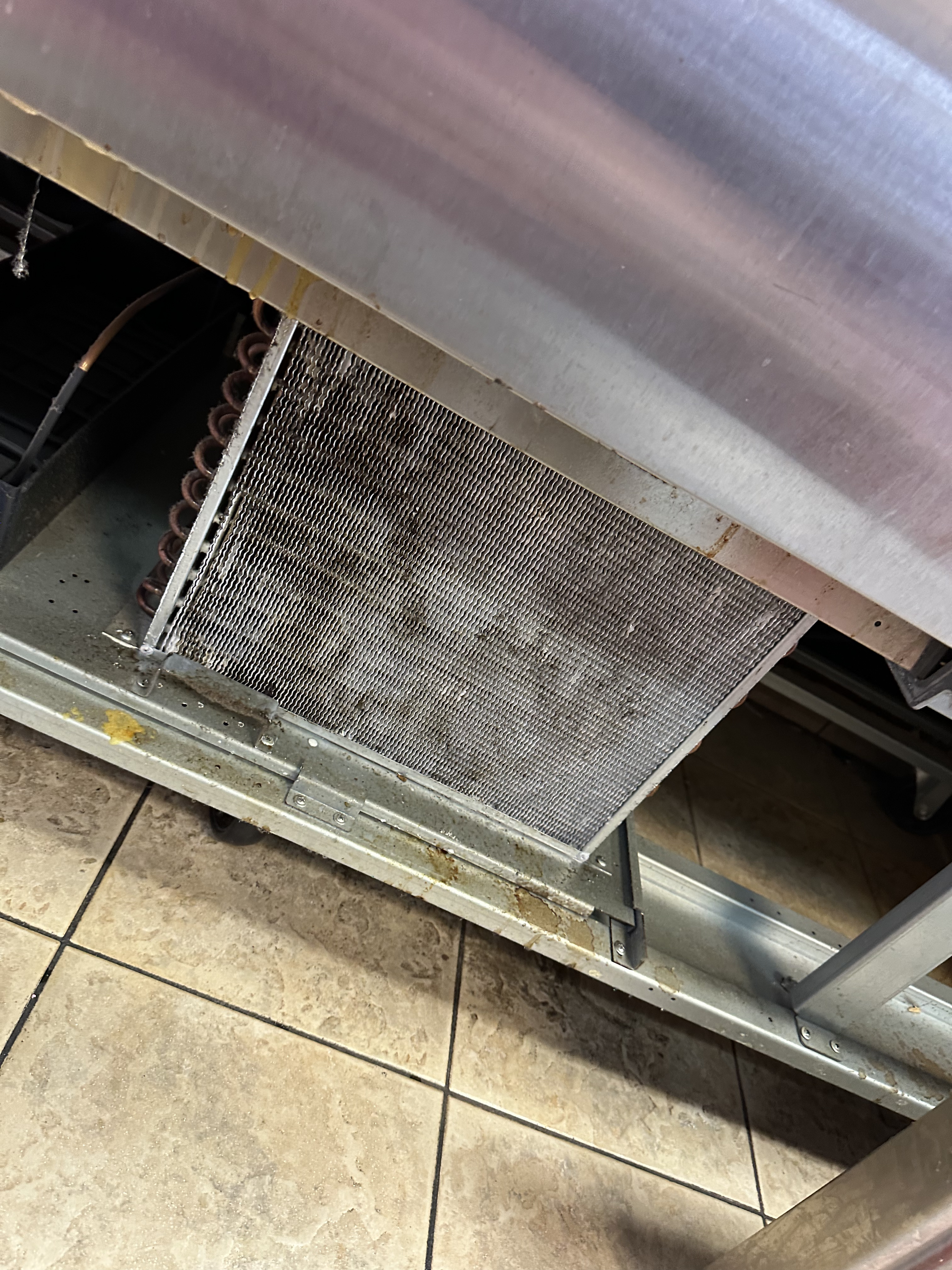 Close-up of an industrial cooler or heat exchanger unit with visible metal fins and coil, situated on a tiled floor.