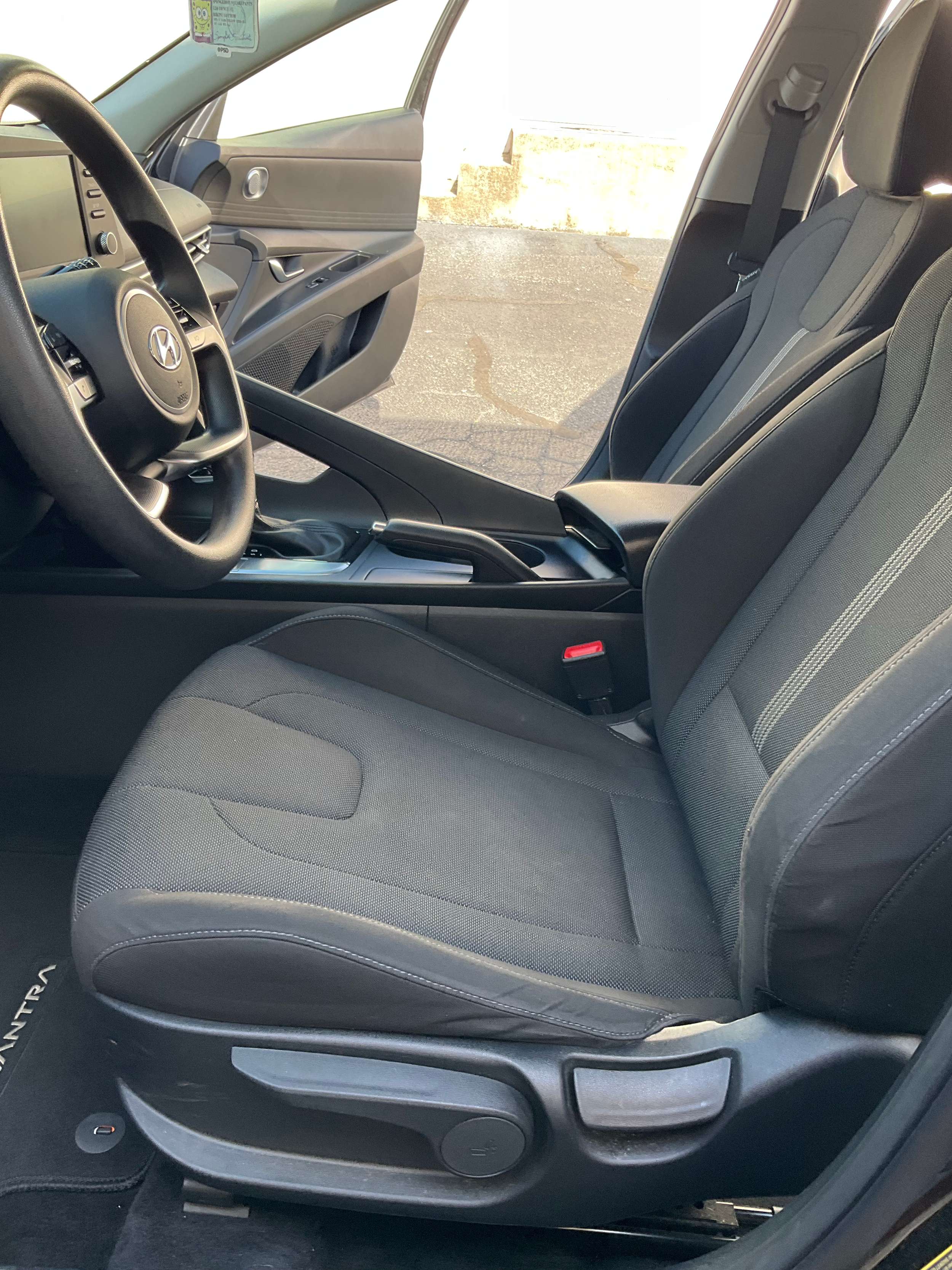 Interior of a car showing the front passenger seat, front door open, and steering wheel, featuring black upholstery and a Hyundai logo on the steering wheel.
