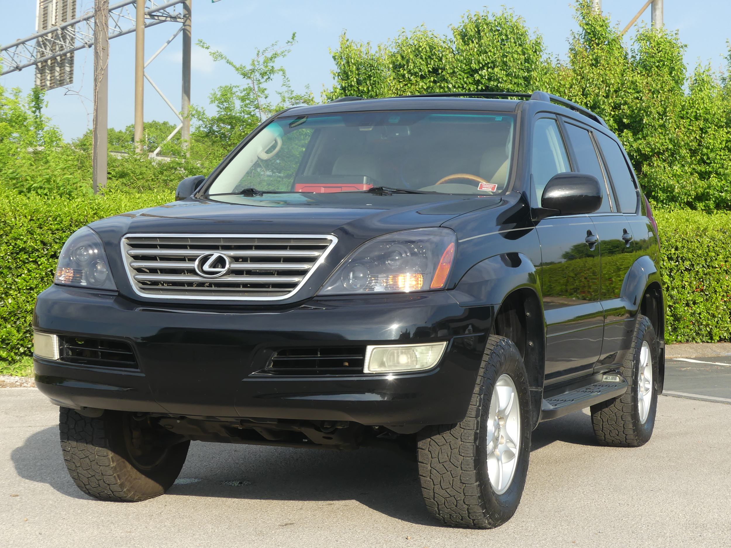 Black Lexus SUV parked outdoors with greenery in the background.