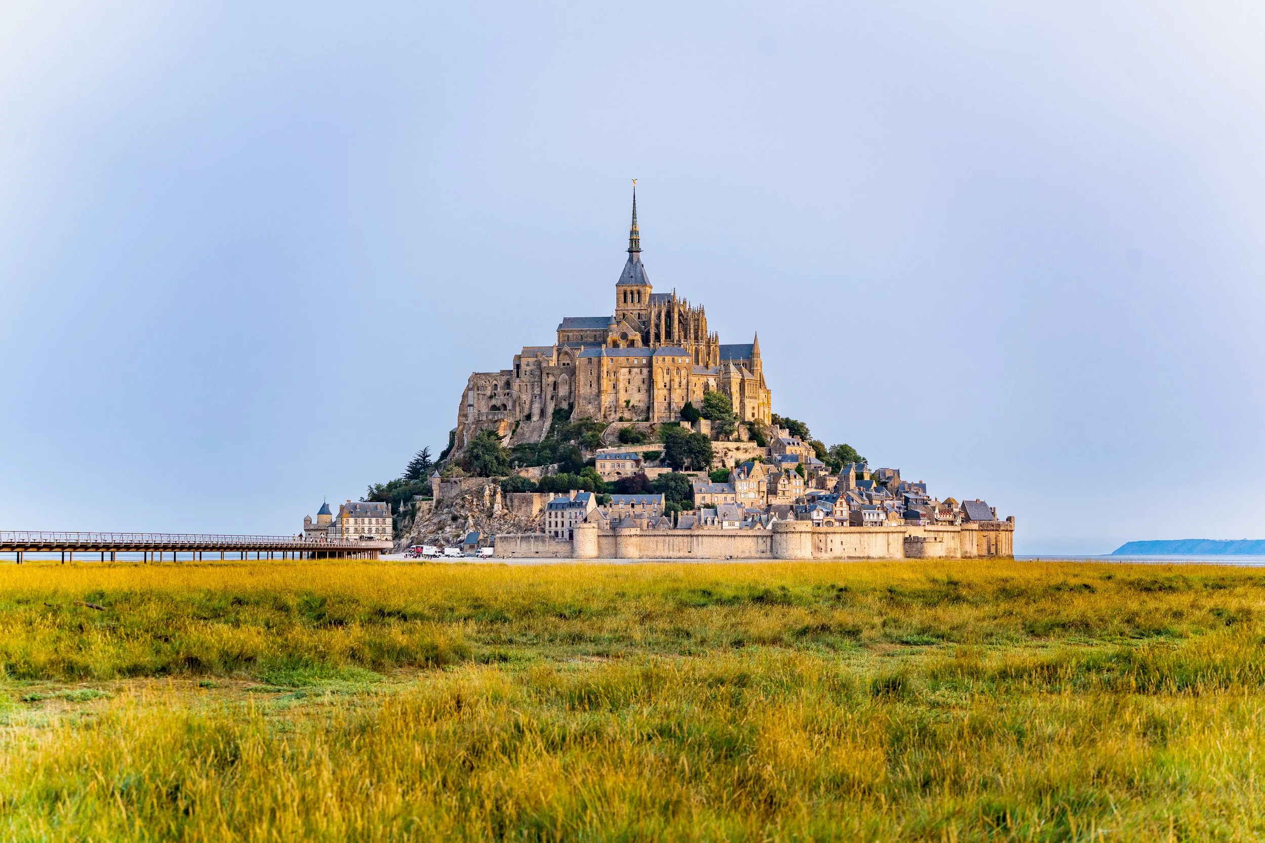 Mont Saint-Michel vue sur la baie, avec ses bâtiments historiques et son abbaye au sommet, entouré de champs verdoyants.