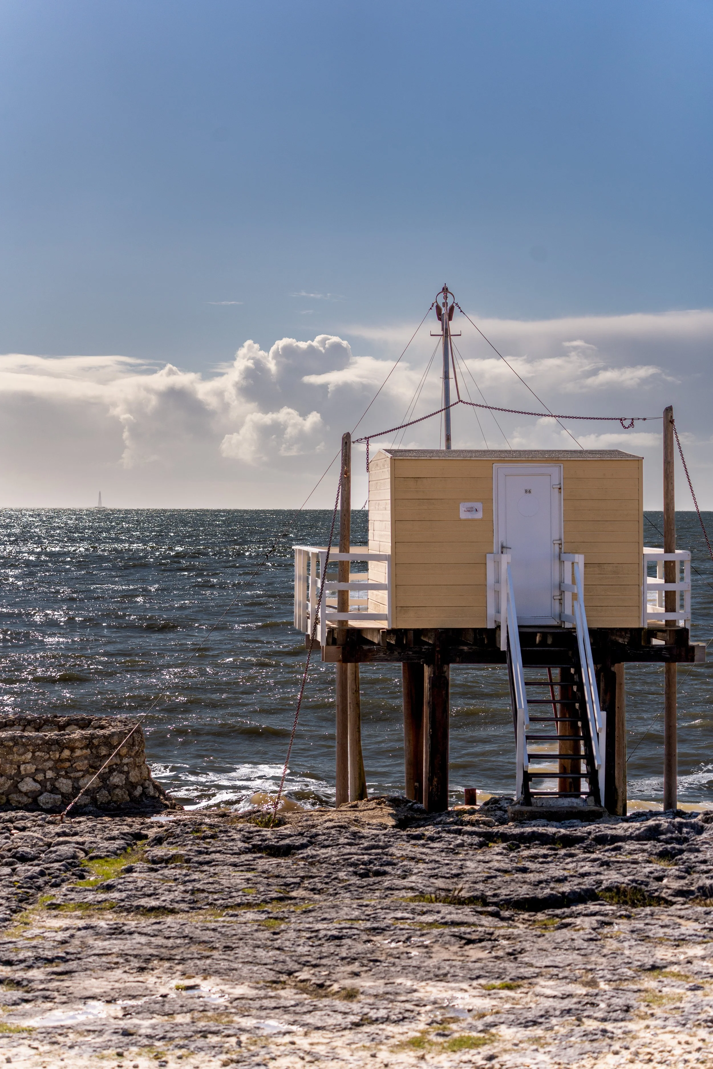 Petit Carelet en bois jaune sur pilotis au bord de l'océan Atlantique avec ciel ensoleillé et nuages.