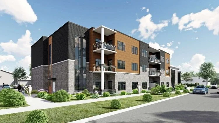 Modern multi-story apartment building with balconies, surrounded by green lawns and trees, under a partly cloudy sky.