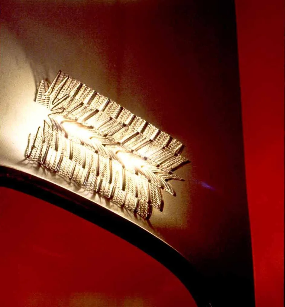 Close-up of a ceiling light fixture designed to look like a leaf, mounted on a red wall.