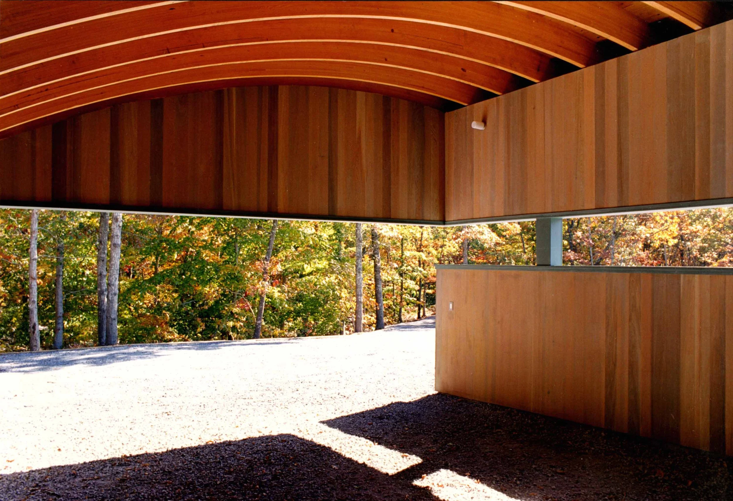 Interior view of a carport with a curved roof surrounded by autumn trees.