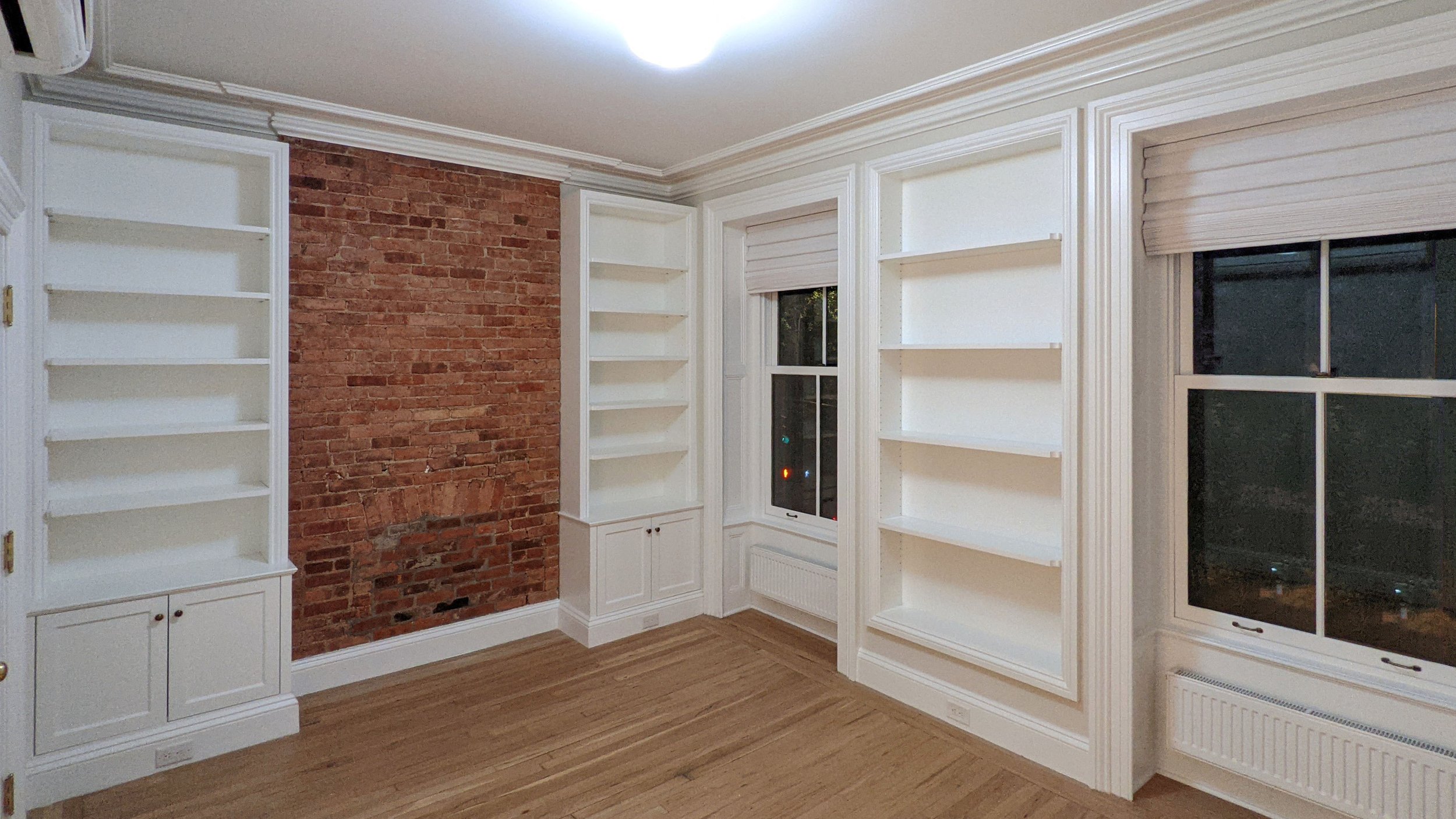 Room with white built-in bookshelves, a window with blinds, and an exposed brick accent wall.