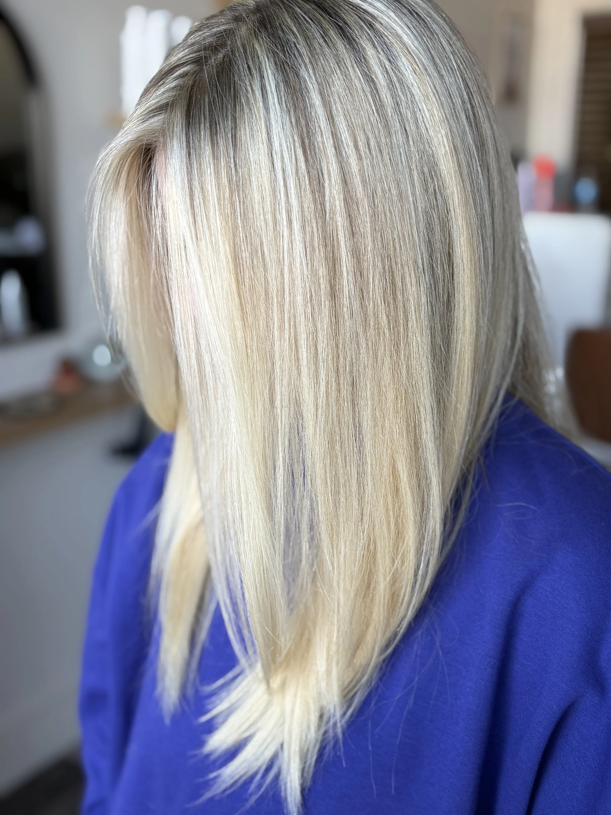 Close-up of a woman's blonde hair, straight and shiny, with a mixture of light and dark blonde shades, partially covering her face.