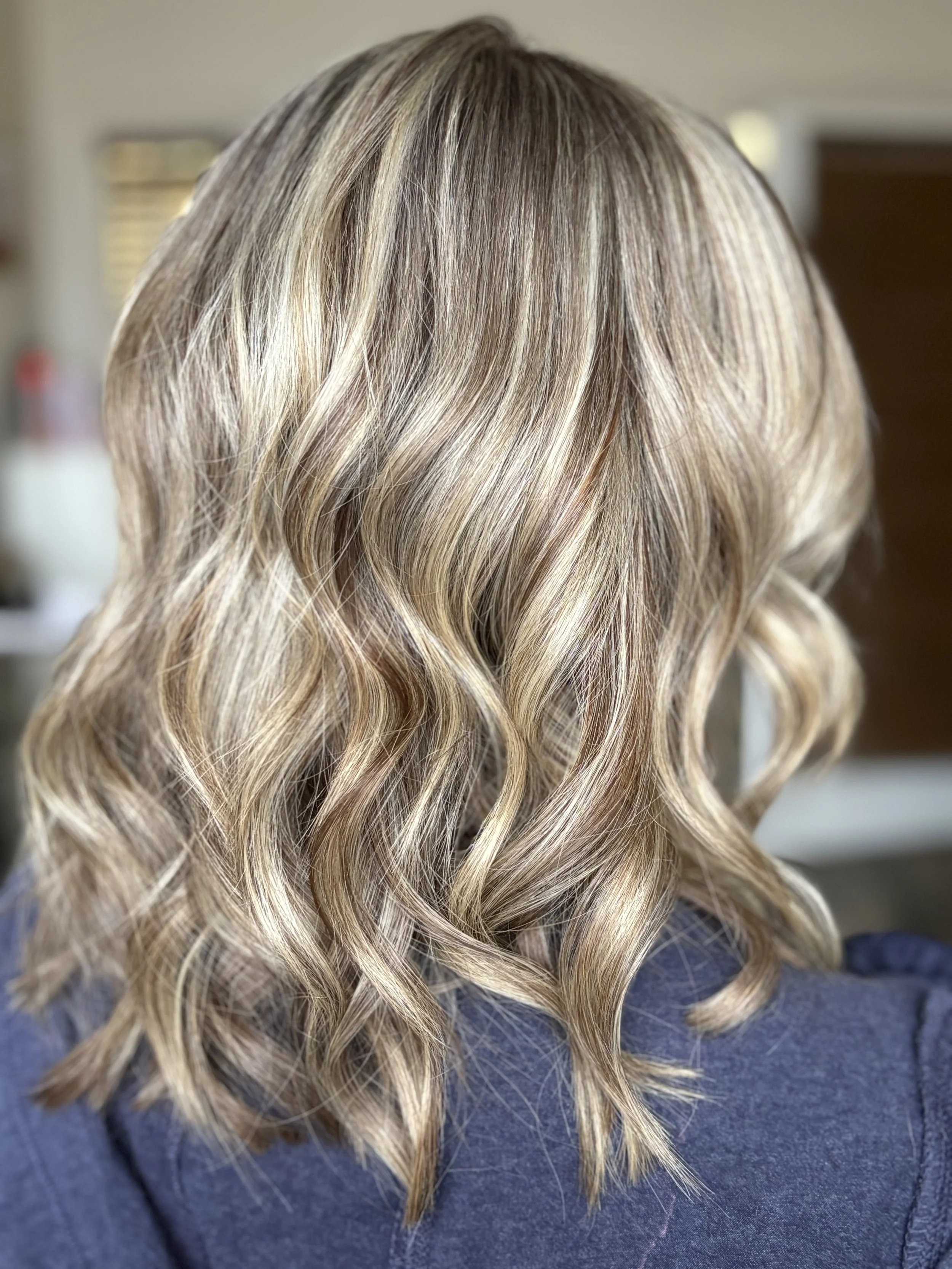 Back view of a woman with shoulder-length, wavy blonde hair.