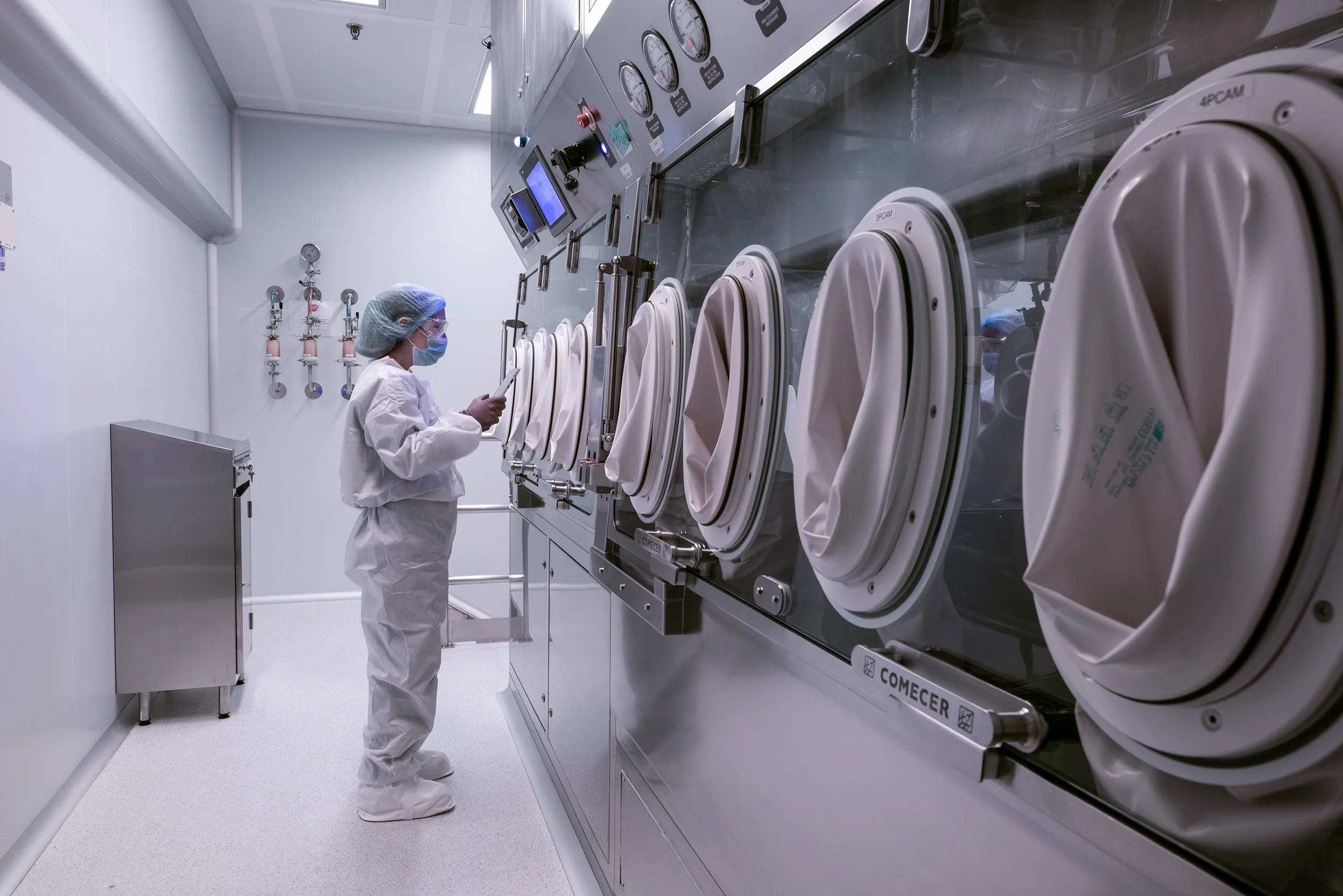 A technician in full PPE operates a row of pharmaceutical isolators in a cleanroom at a GSK manufacturing facility designed by Bryden Wood