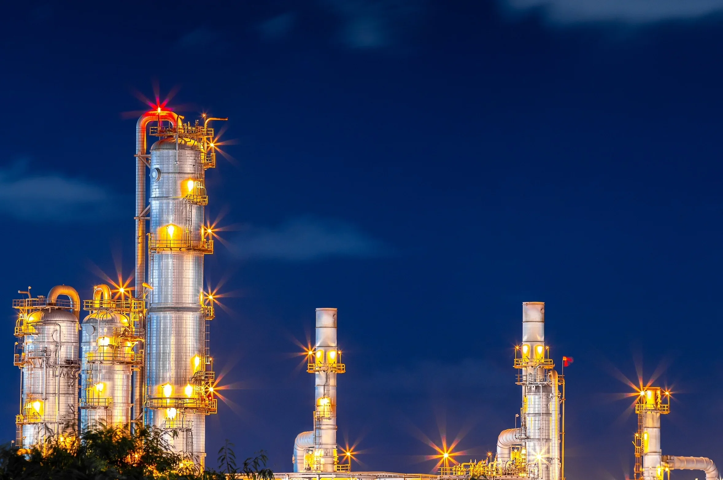 Lit distillation columns and process towers at a chemical plant against a night sky, representing large-scale solvent production and processing infrastructure