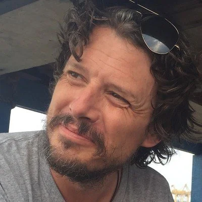 Man with curly hair and beard wearing sunglasses on head looking to the side
