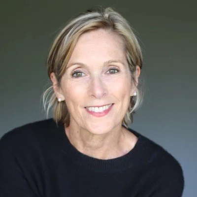 Smiling person with short hair wearing a black sweater, posing against a plain background.