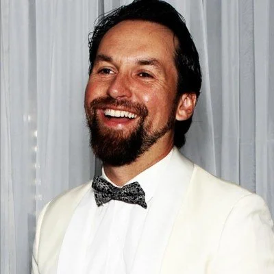 Man in a white suit with a bow tie smiling