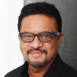 A man with dark close cropped hair, wearing glasses and a black shirt