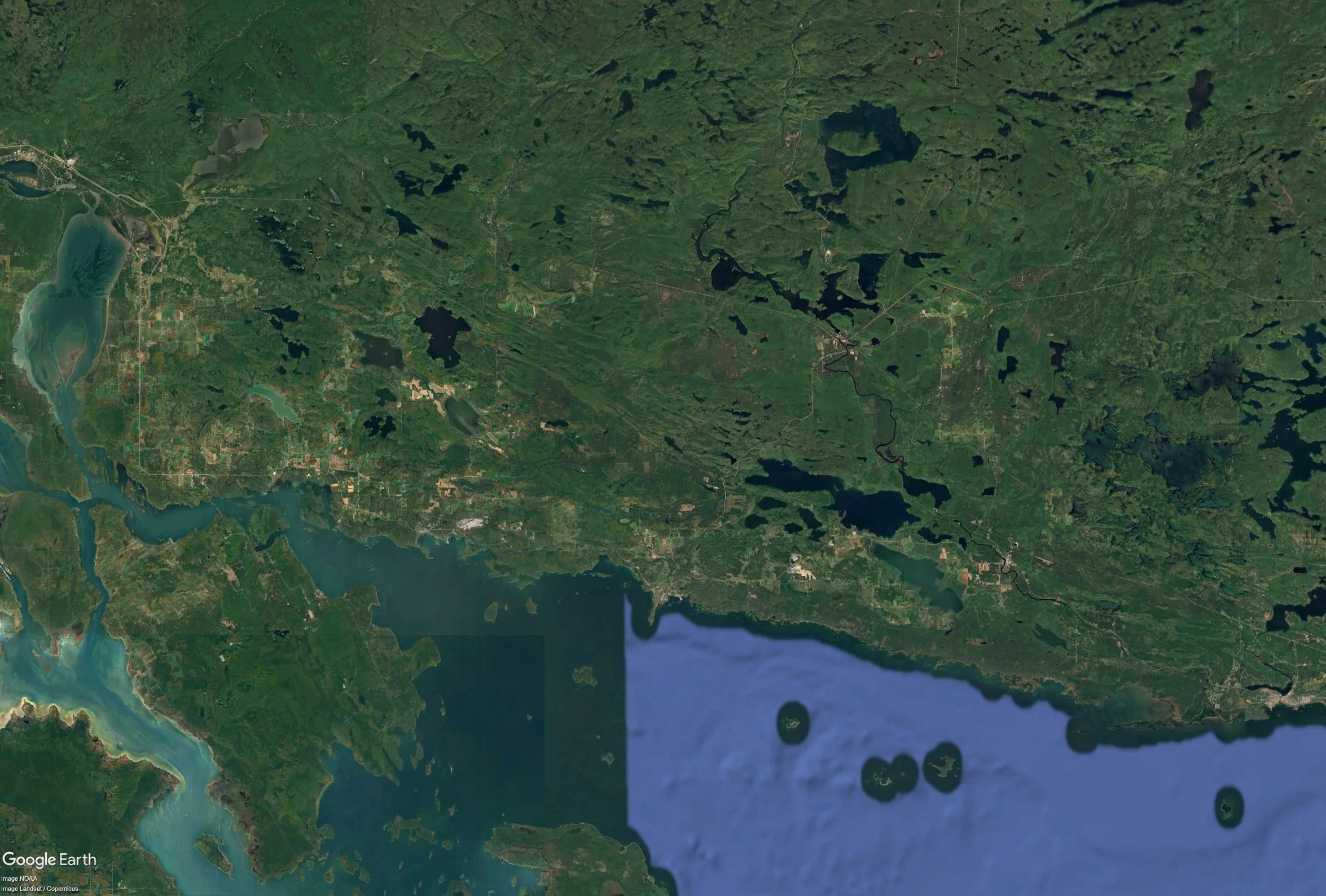Satellite view of a large body of water with numerous islands, surrounded by green land and water reservoirs, with some urban areas visible.