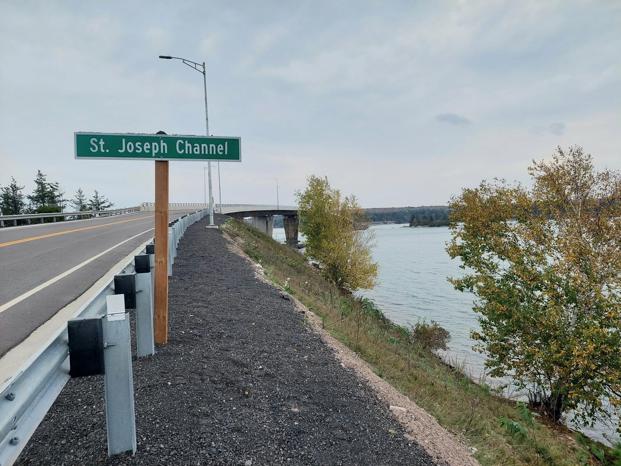 A road on a bridge over a river with trees on the riverbank and a street sign that says 'St. Joseph Channel'.