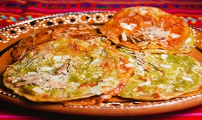 Three tlayudas with refried beans, cheese, lettuce, and salsa on a decorative plate.