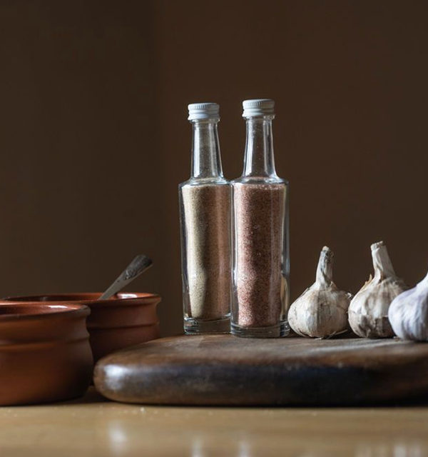 Two glass bottles filled with salt and garlic cloves on a wooden surface.
