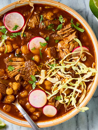 A bowl of beef and chickpea stew garnished with radish slices, chopped cilantro, and shredded cabbage.