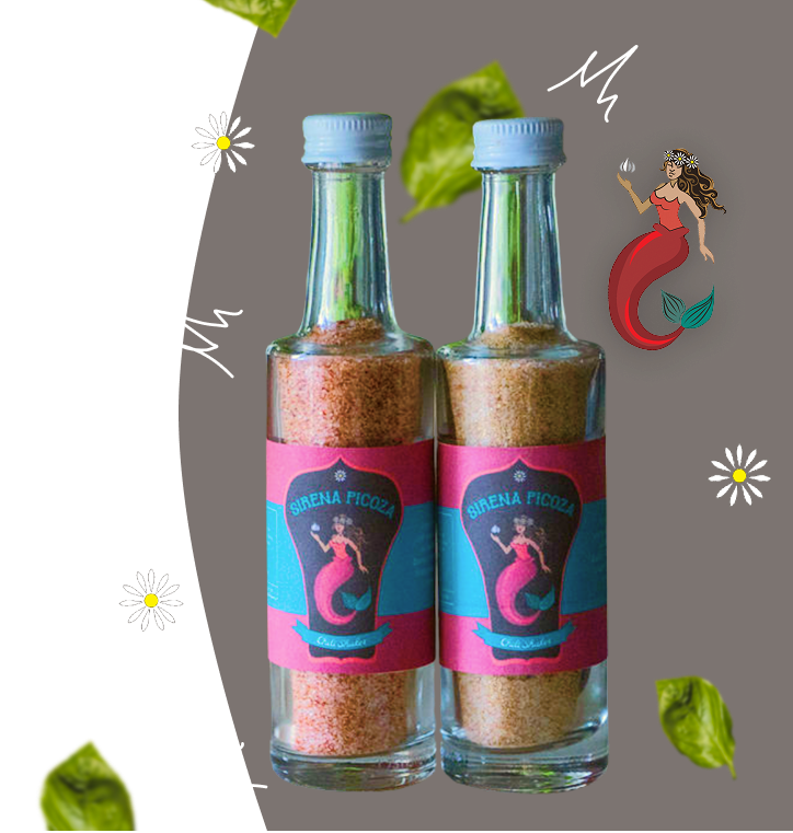Two glass bottles with pink and blue labels reading 'Sirena Picoza' and containing a pinkish seasoning or powder, set against a dark background with decorative flowers, leaves, and a mermaid illustration.
