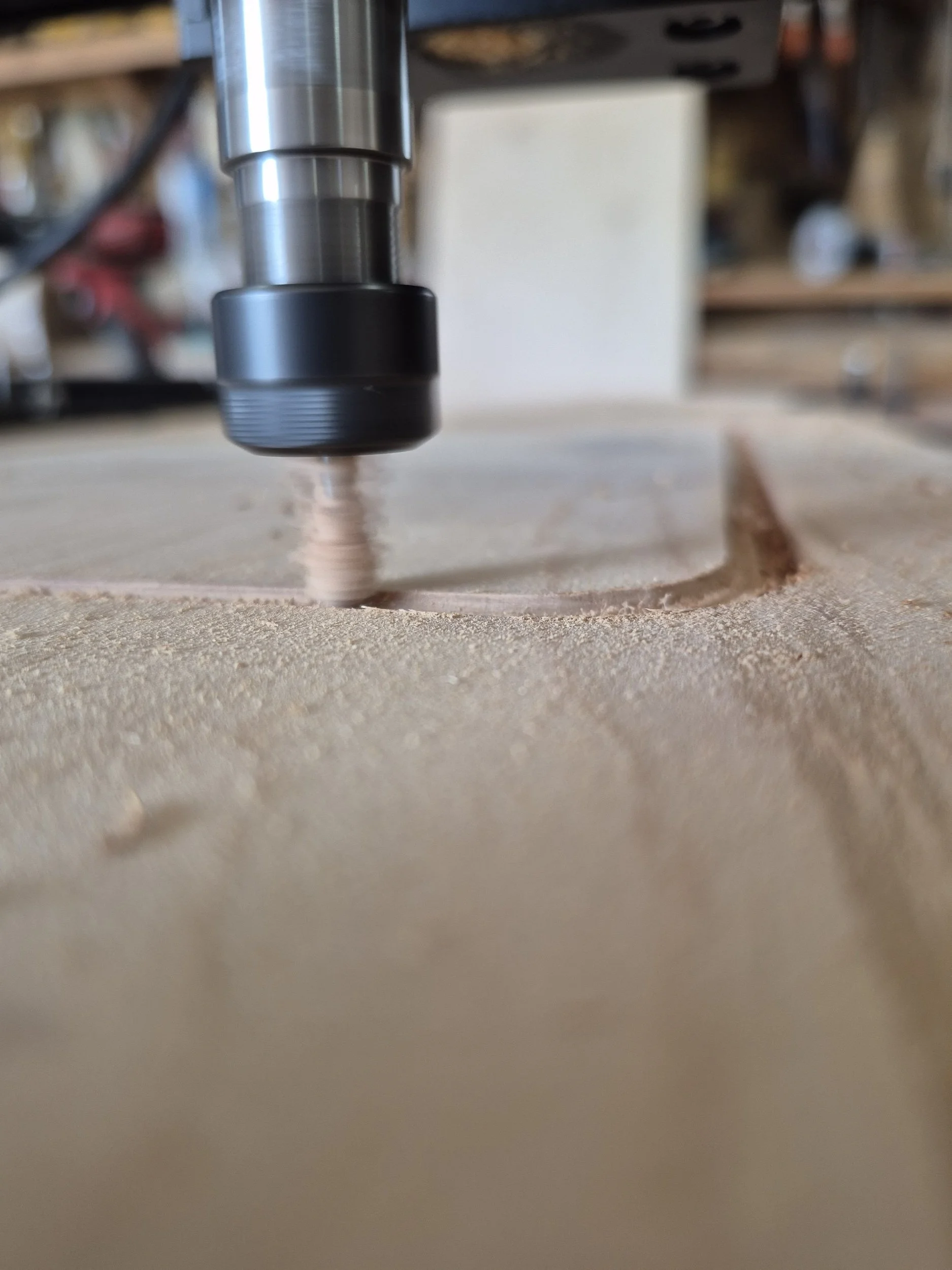 Close-up view of a CNC or router machine drill bit carving a rectangular cutout in a piece of wood, with wood dust around the cut.