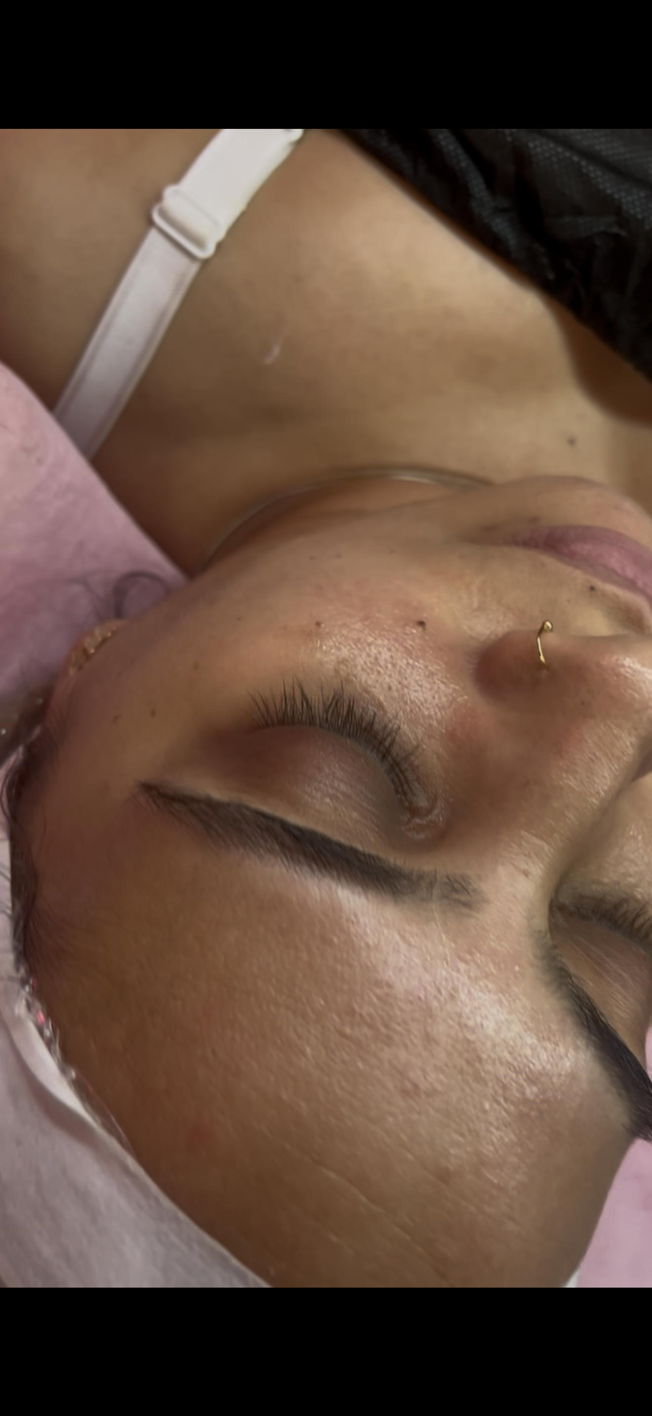 Close-up of a woman's face and upper chest, with her eyes closed and head tilted back. She has a nose piercing, long eyelashes, and textured skin.
