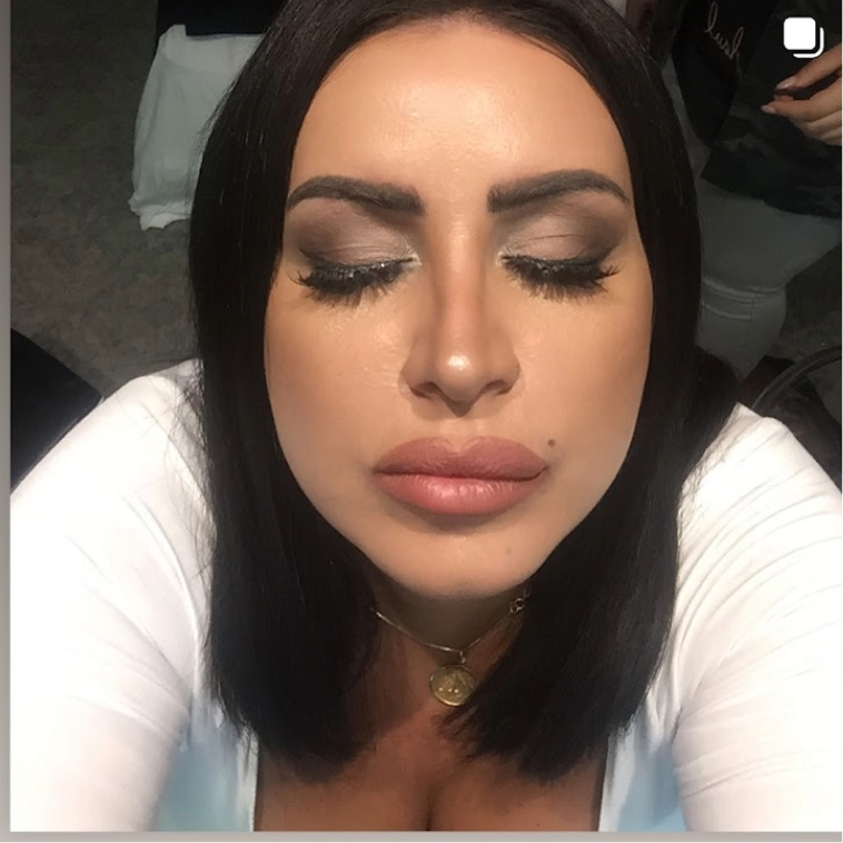 Close-up of a woman with dark hair, makeup, and a white top, eyes closed, and a gold necklace.