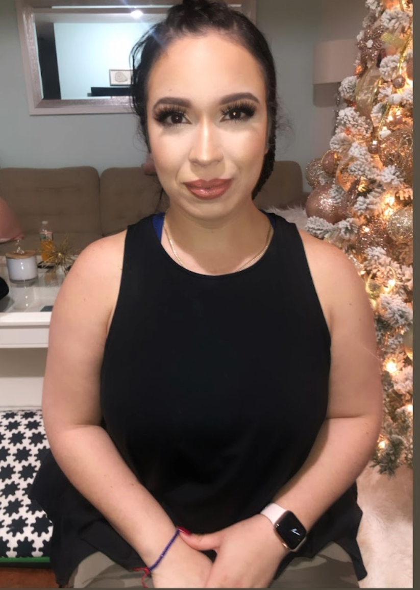 A woman sitting indoors next to a decorated Christmas tree with white and gold ornaments and lights.
