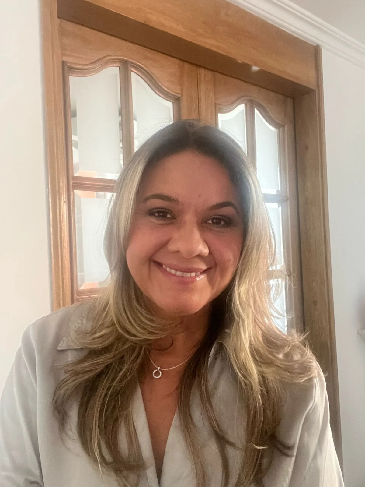 Woman smiling indoors with wooden door in background.