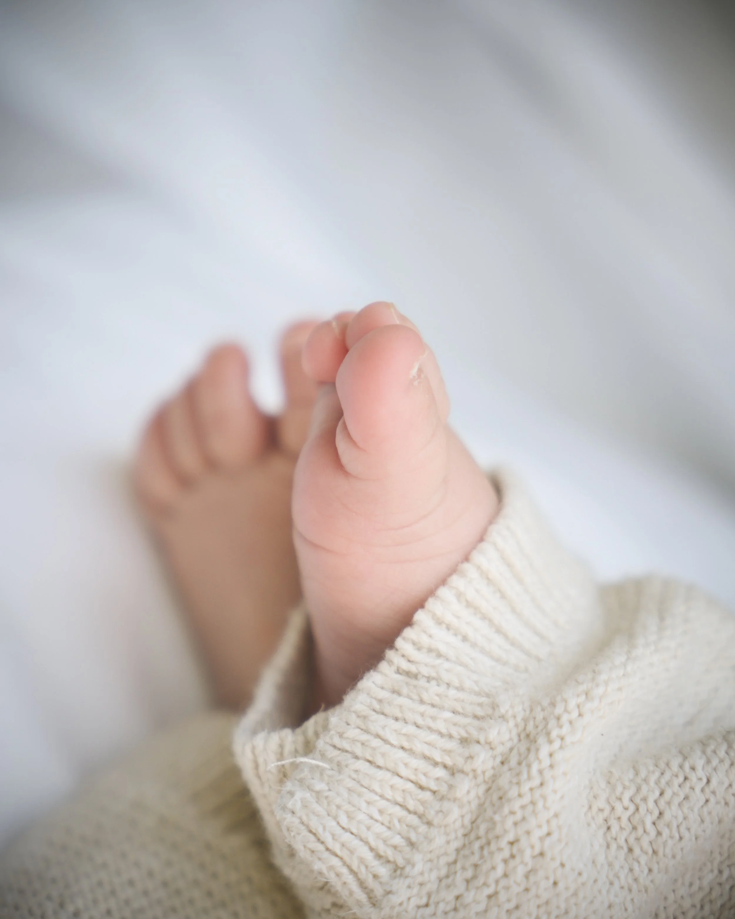 Close-up of a small baby's foot with toes, wearing a beige knitted sock.