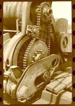 Close-up of industrial machinery with gears, chains, and pulleys in sepia tone.