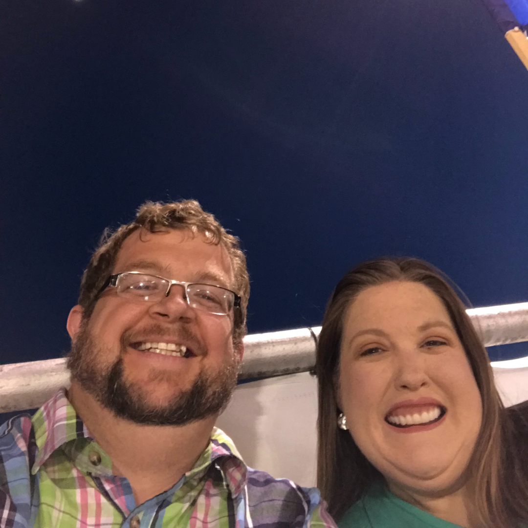 A man and woman smiling at night, taking a selfie outdoors.