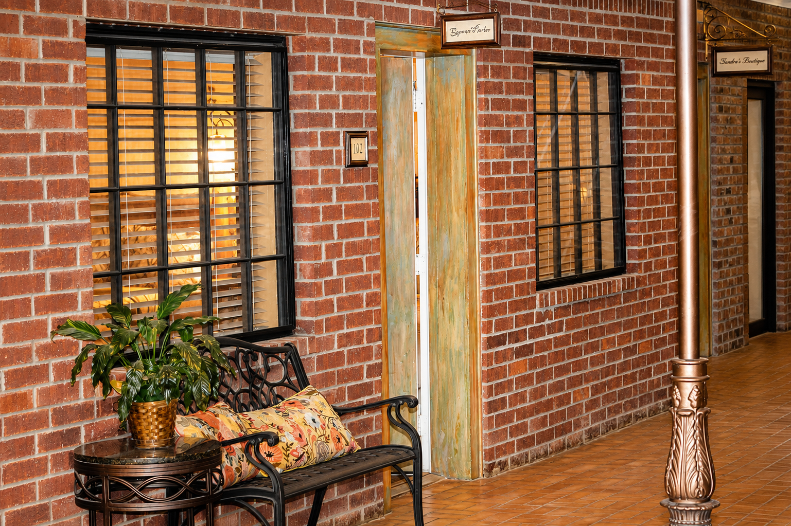 Brick wall with two windows, a bench with a cushion and a plant, a wooden door, a decorative streetlamp, and small signs indicating shops. Nocona Texas Red River Inn