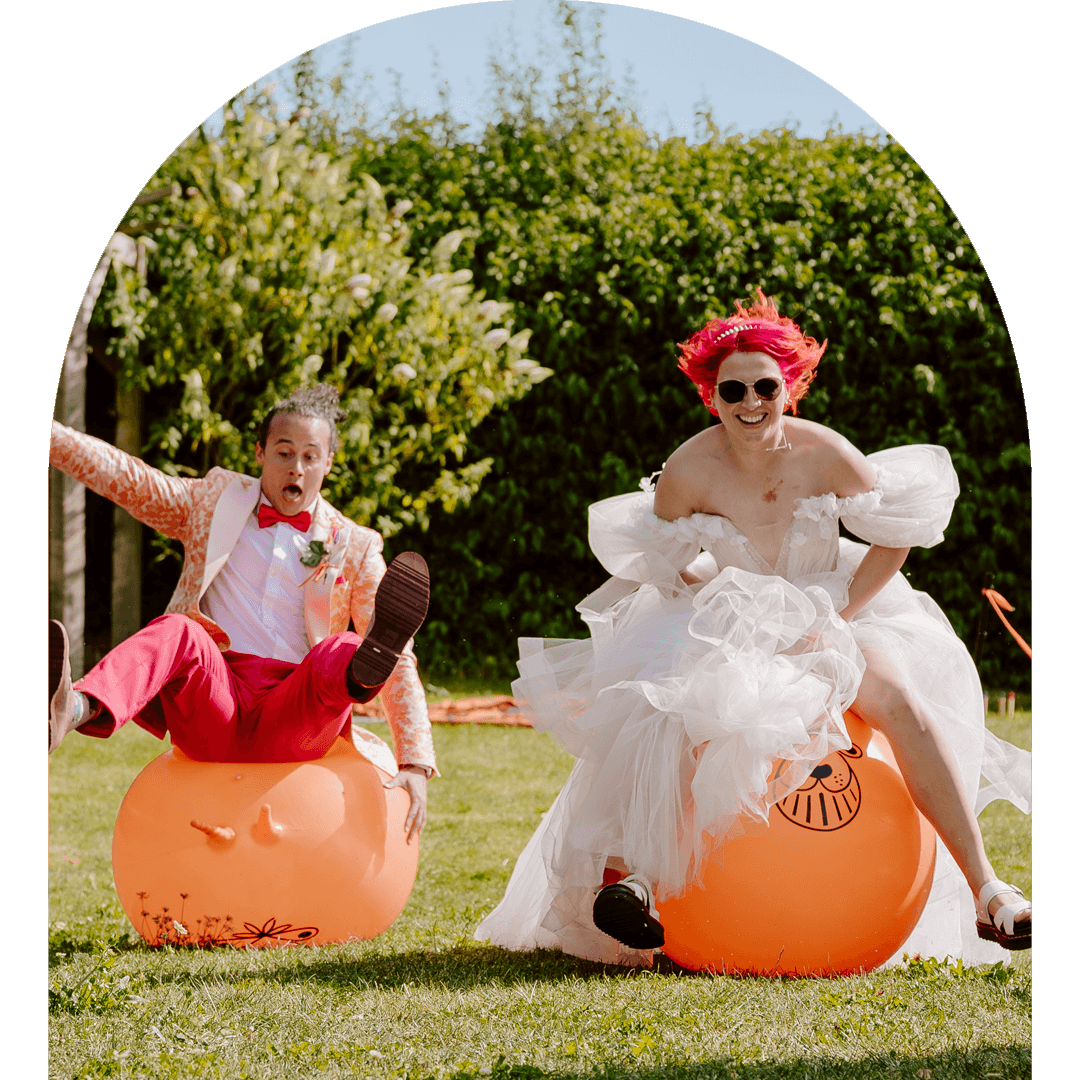 Hollie and her husband are racing space hoppers. Hollie is bouncing along in her poofy dress and laughing and A-Jay is dramatically falling behind her