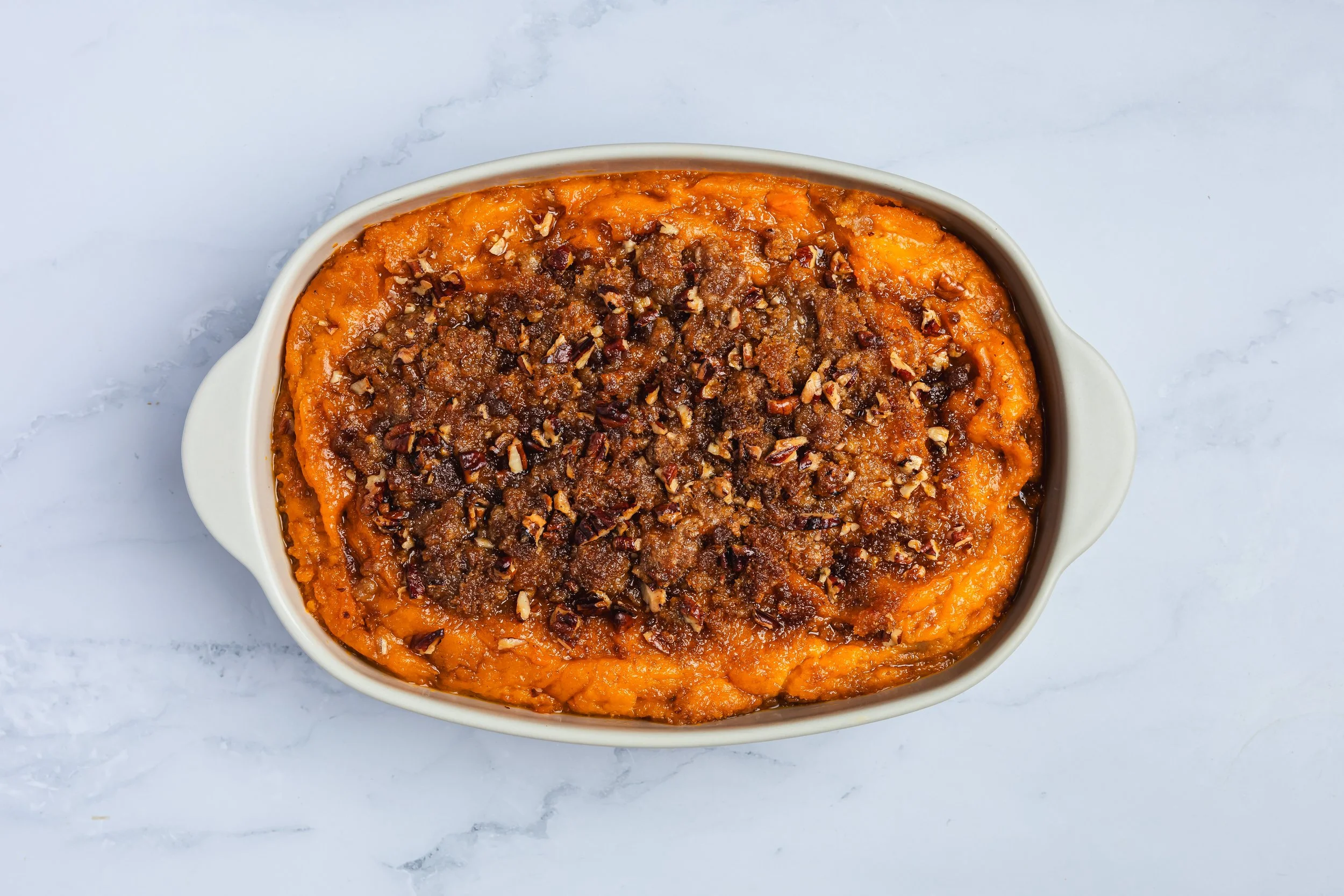 Sweet potato casserole topped with chopped pecans in a white baking dish