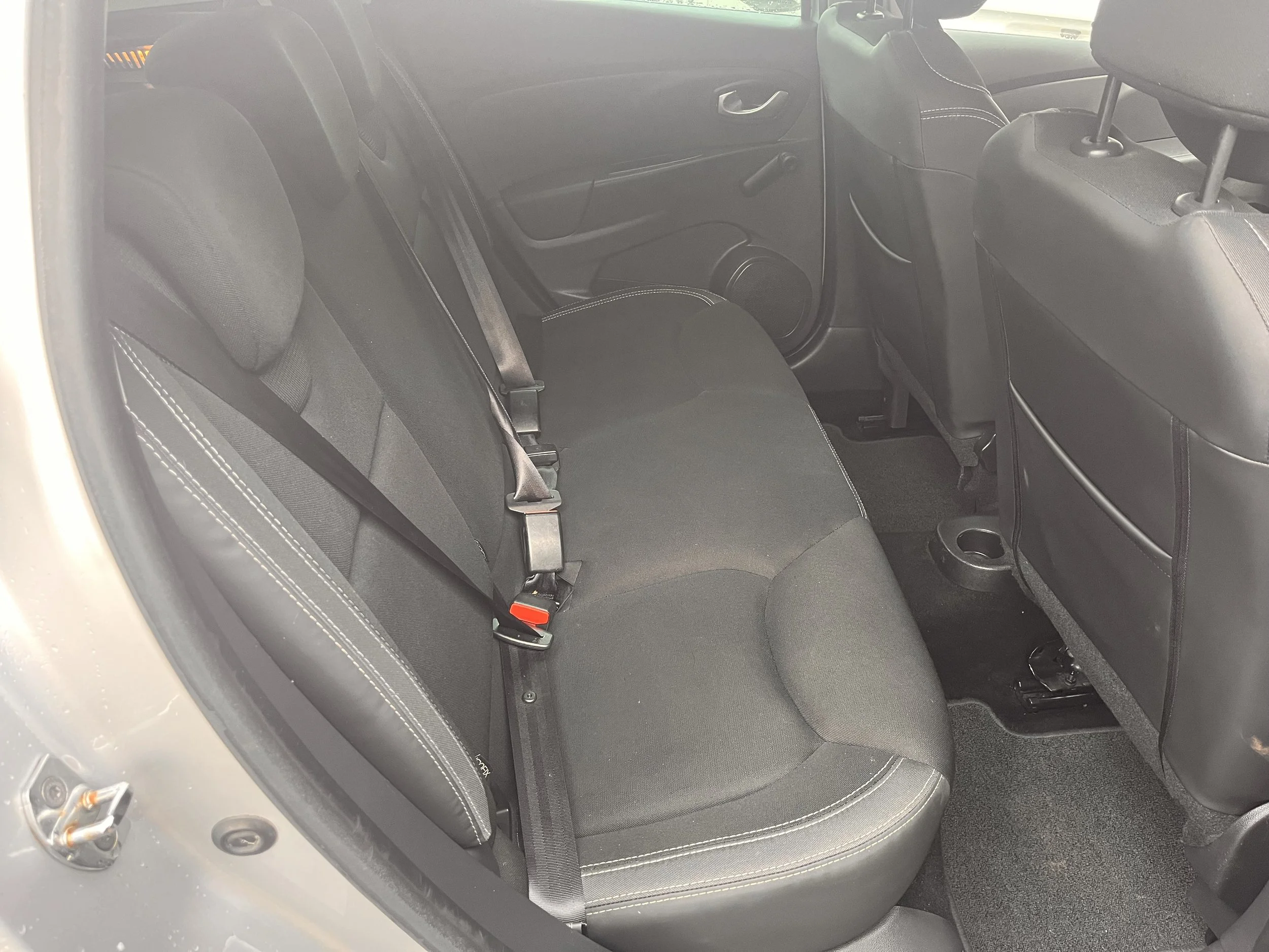 The interior of a car showing the back seats with seat belts, headrests, and part of the front seats and dashboard.