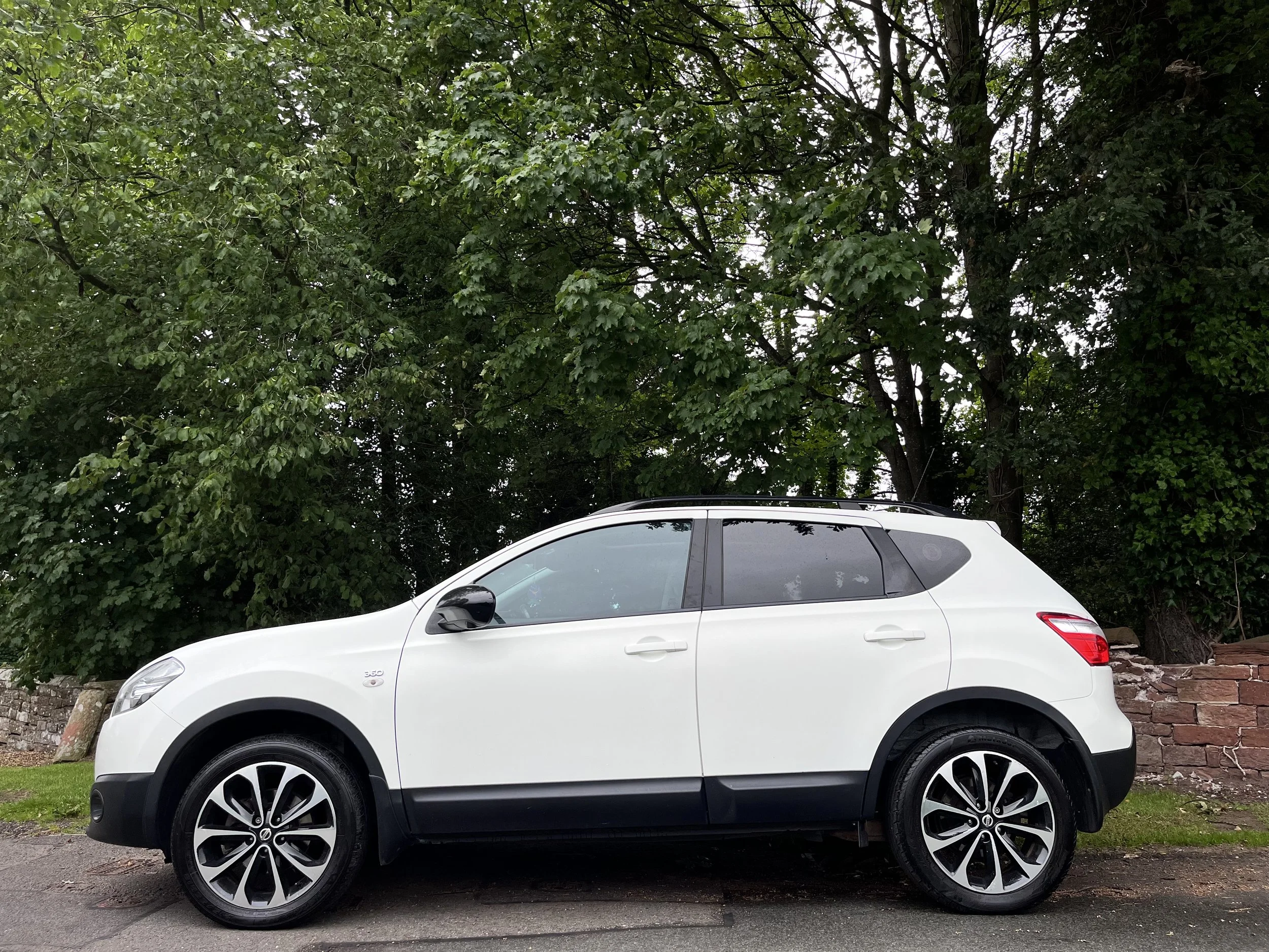 White compact SUV parked on a street with green trees in the background.