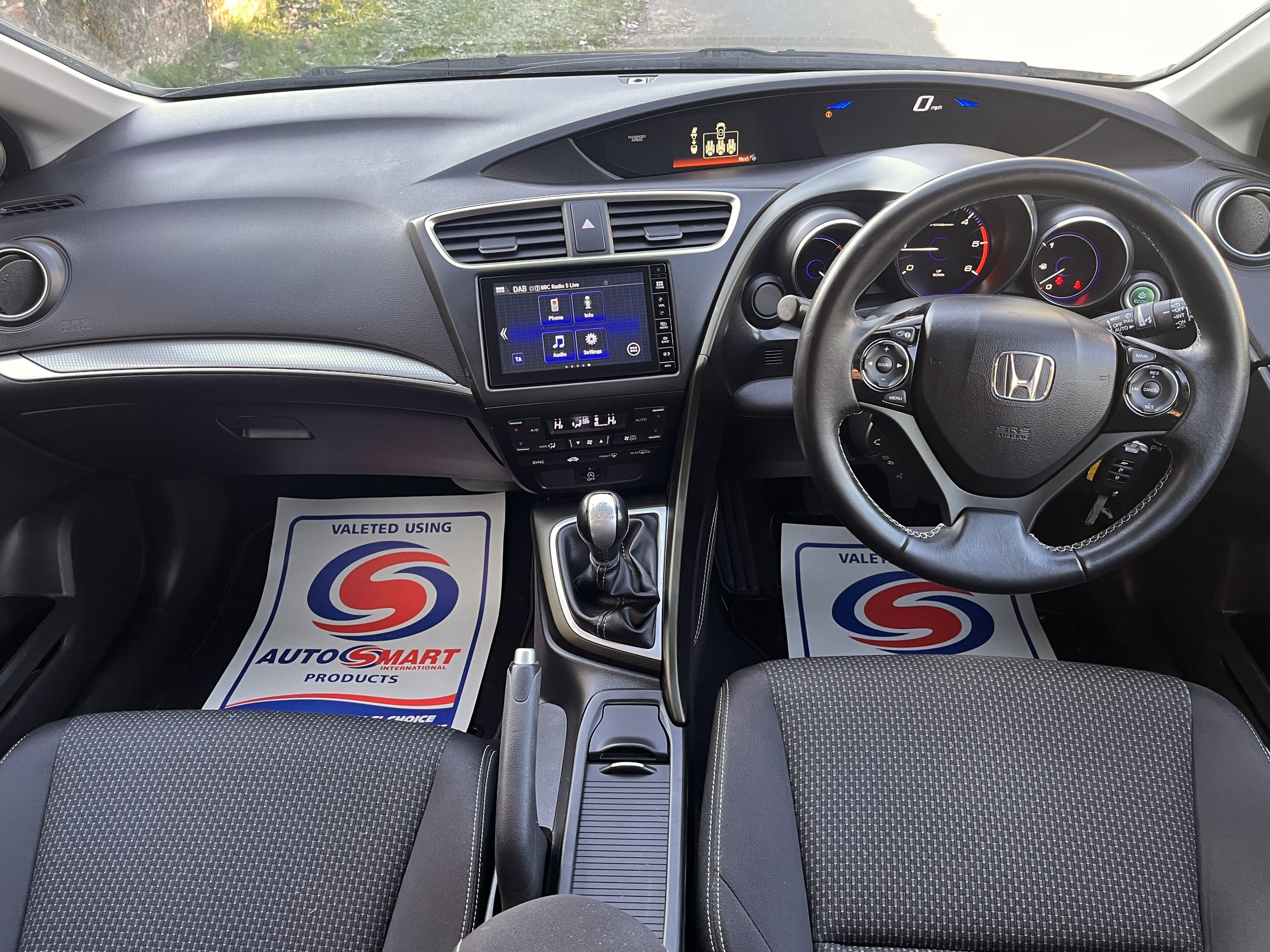Interior of a Honda vehicle showing the dashboard, steering wheel, gear shift, and two front seats with mats displaying 'Valeted Using AutoSmart Products'.
