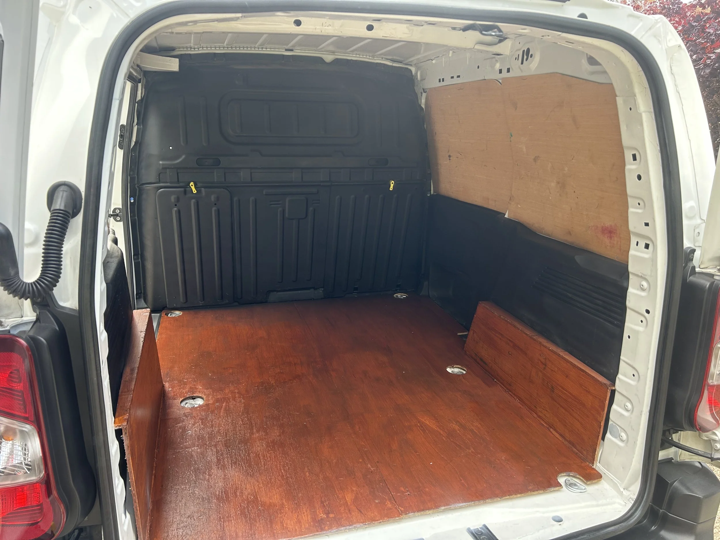 Empty cargo space of a van with a wooden floor and side panels, and black plastic interior lining.