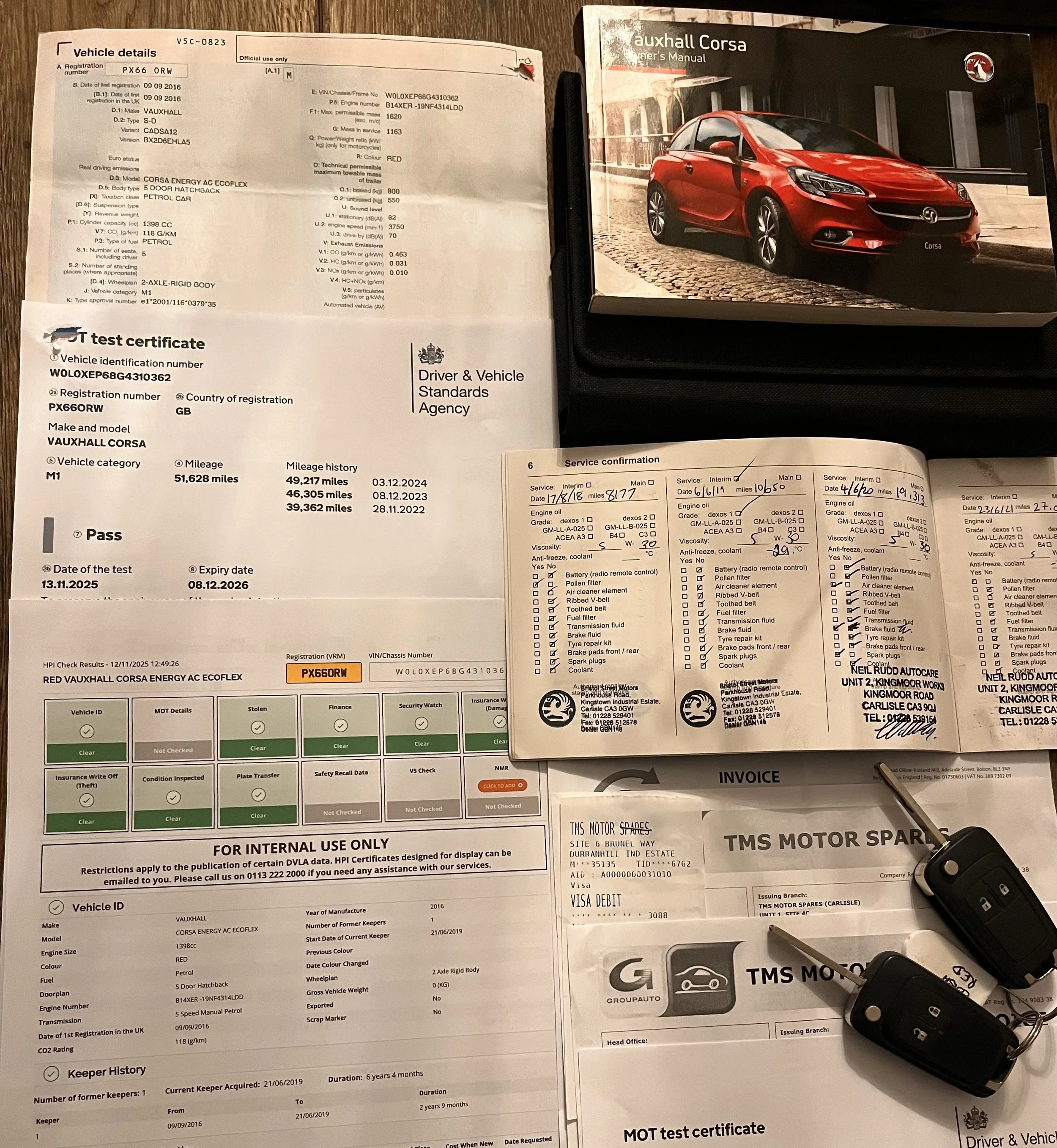 A red Vauxhall Corsa owner's manual, vehicle registration and test certificate, service confirmation documents, an invoice from TMS Motor Spares, and two car keys with remote fobs.