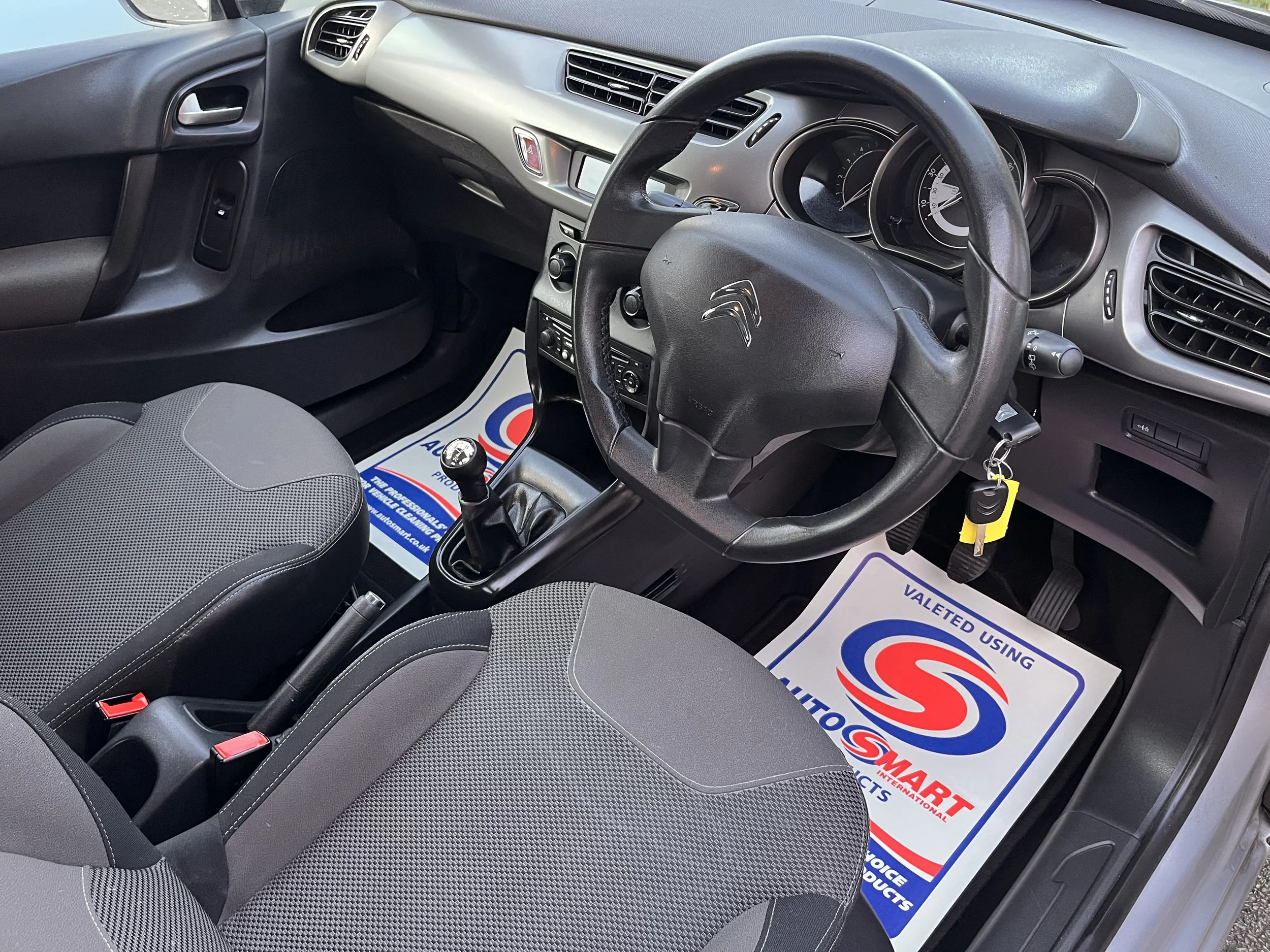 Interior of a grey Citroën car showing the steering wheel, gear shift, driver and passenger seats, dashboard, and floor mats with the AutoSmart logo.