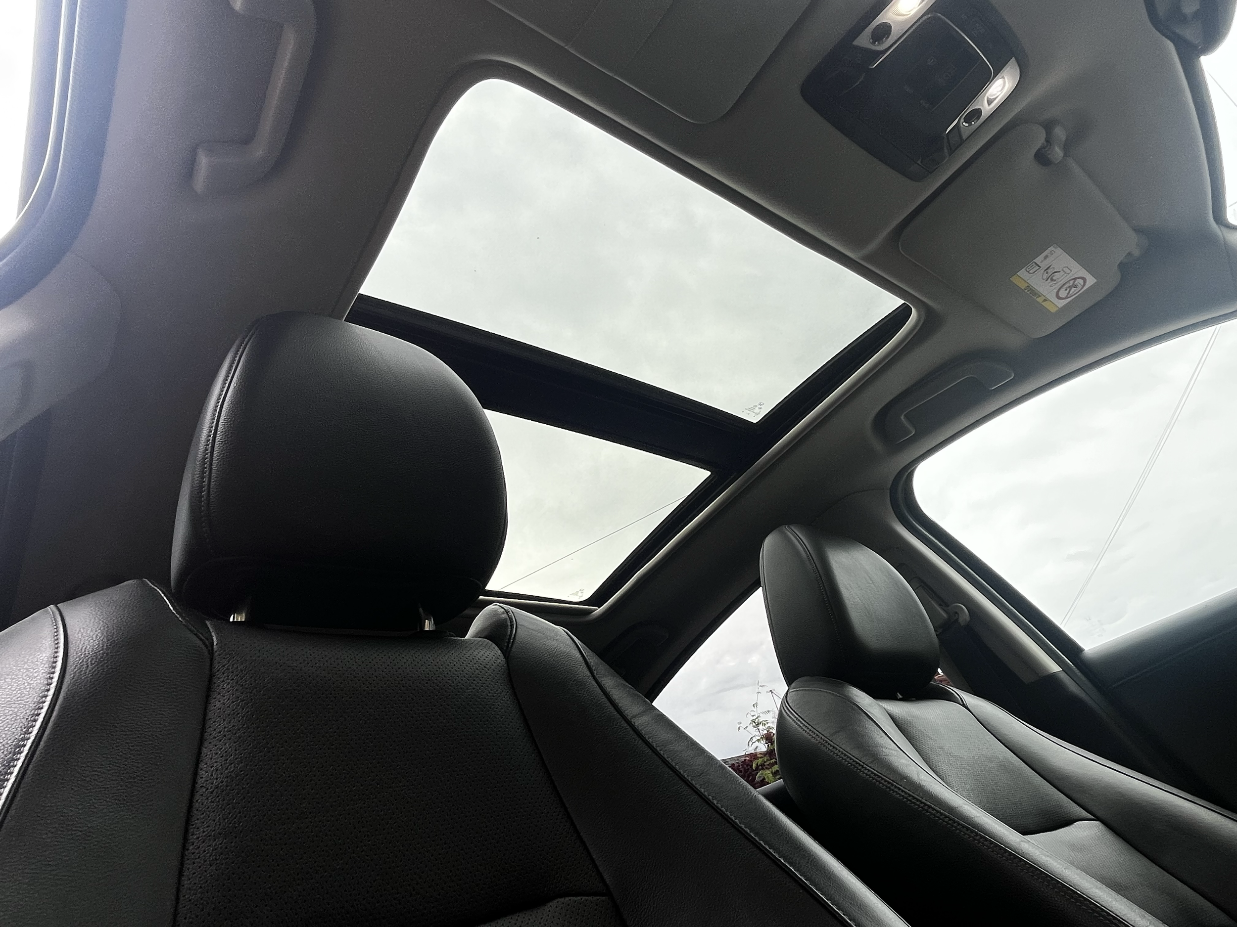 View of the interior of a car showing black leather seats and a sunroof through which the cloudy sky is visible.