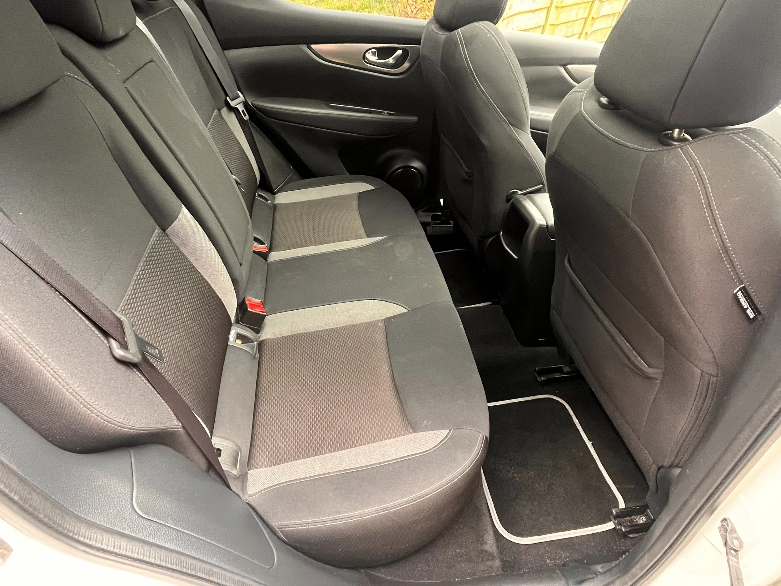 Interior of a car showing two rows of seats with fabric upholstery, a rear door with a window, and black floor mats.