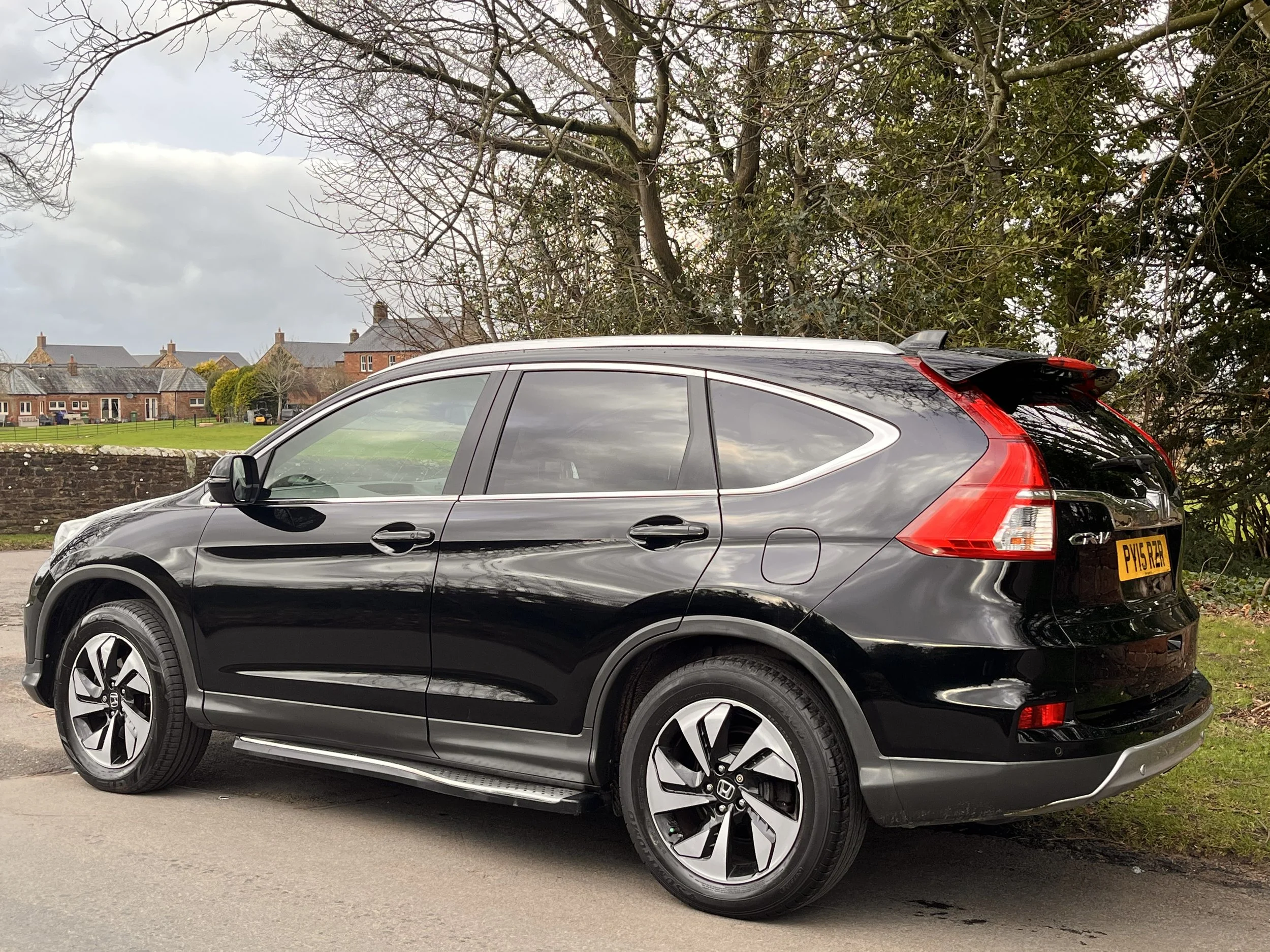 Black Honda CR-V parked on roadside with residential houses and trees in background.
