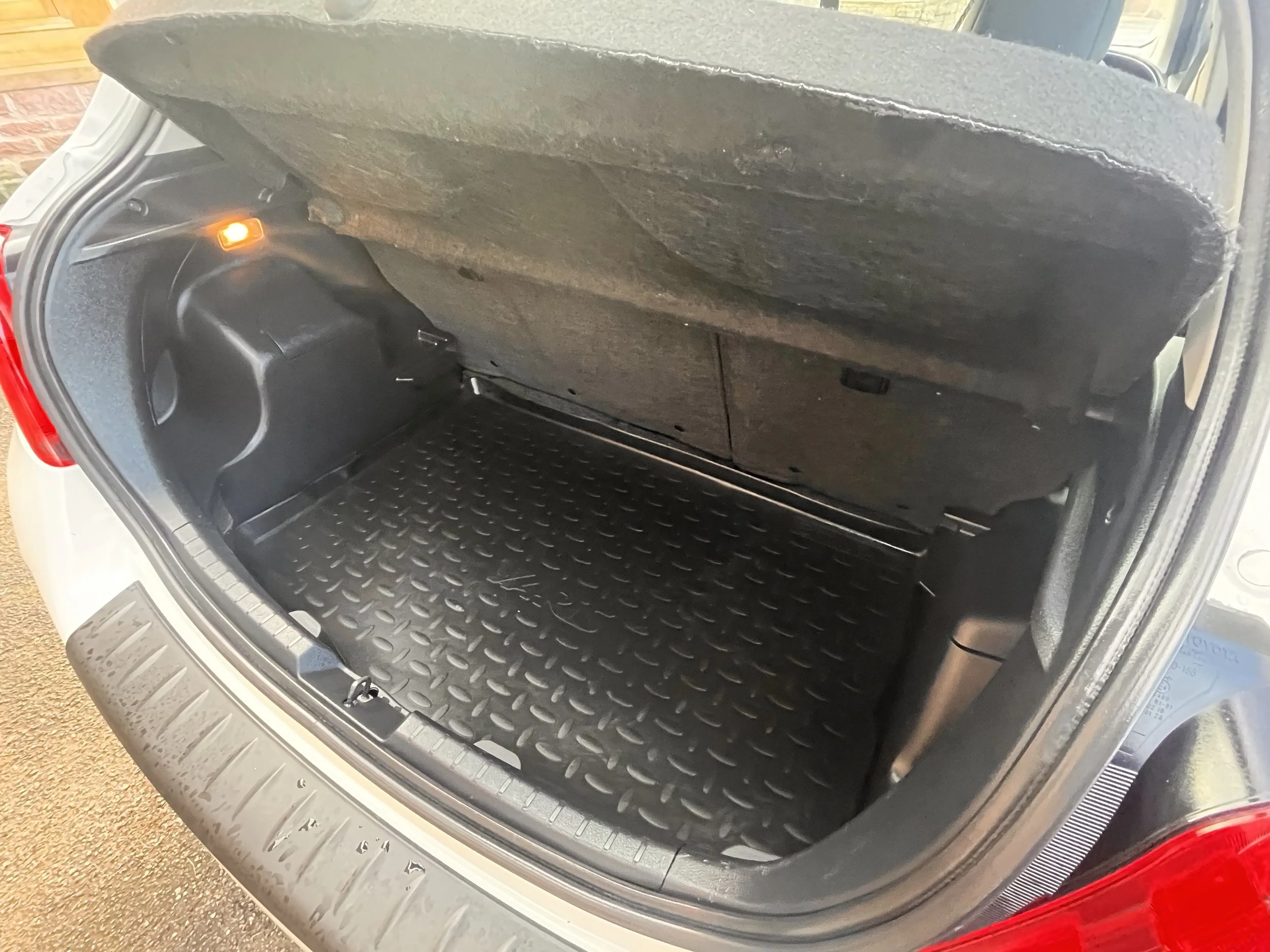 Empty car trunk with a textured rubber mat floor and a partially visible back seat fold-up panel.