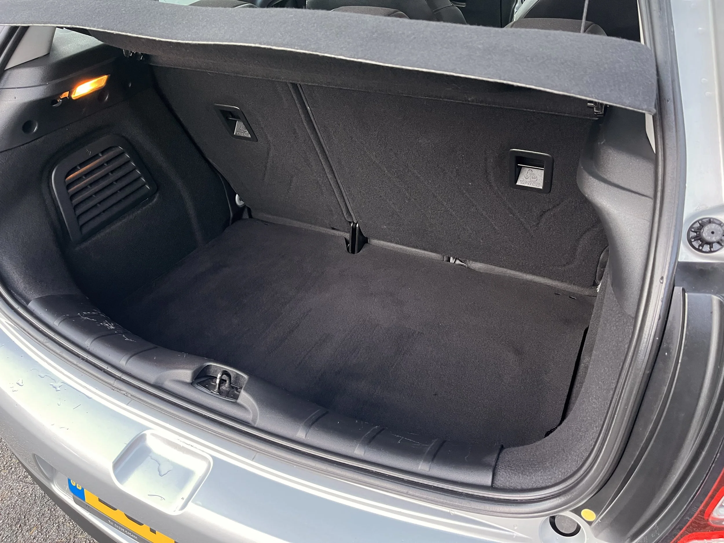 Empty car trunk with black interior, rear seats, and a small orange light on the left side.
