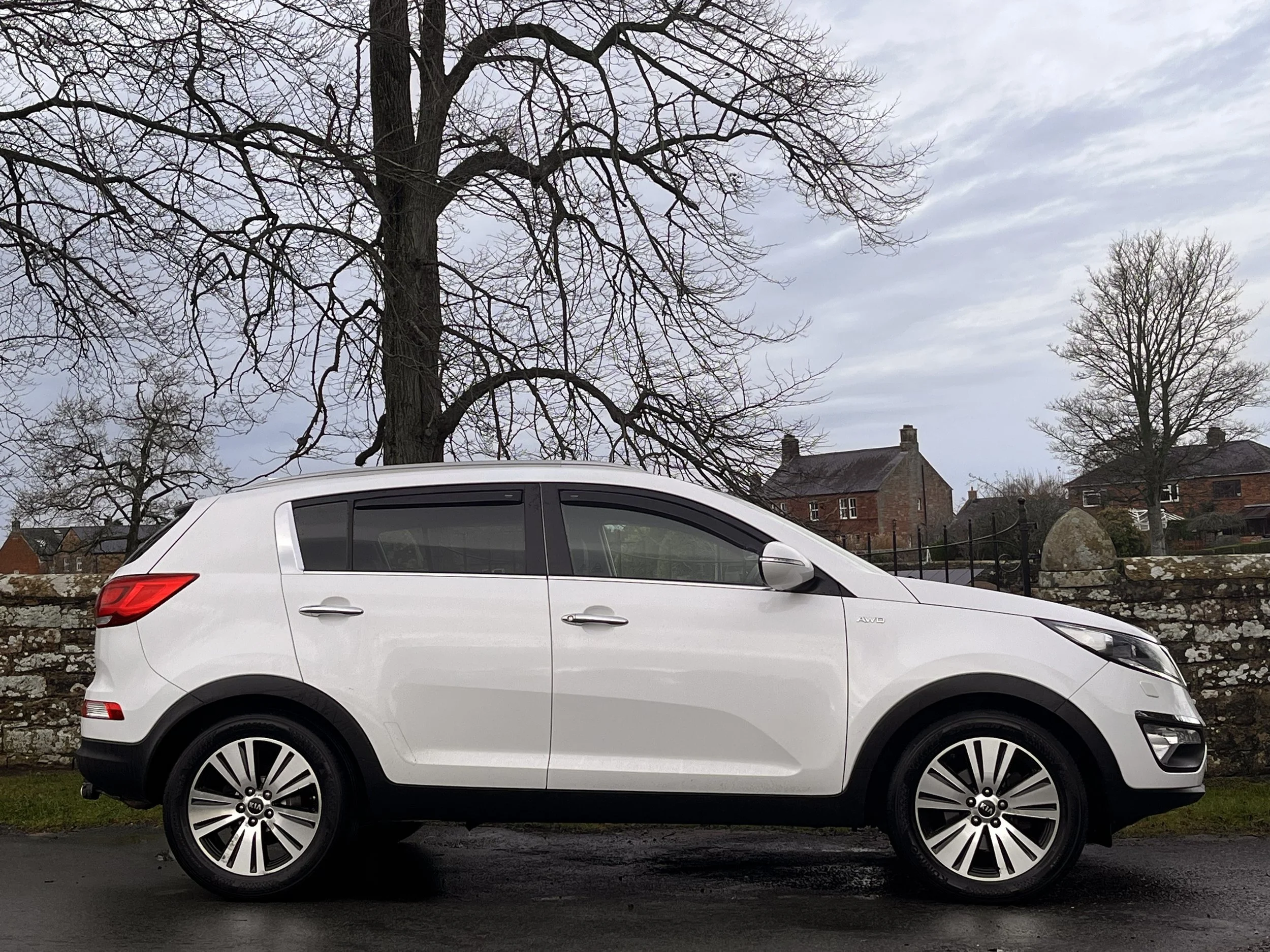 White SUV parked on the street with leafless trees and suburban houses in the background.