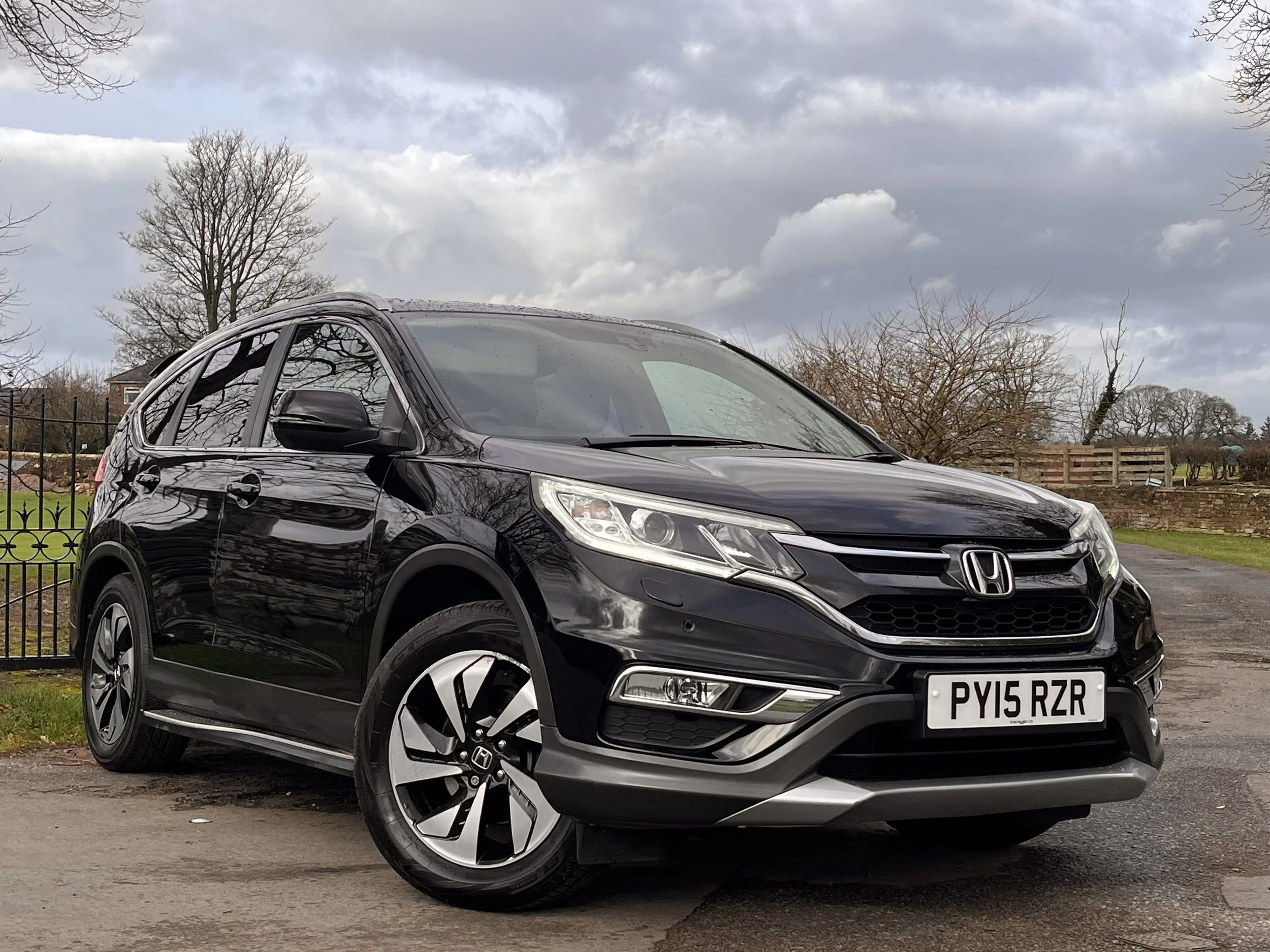 A black Honda HR-V parked outdoors on a paved surface on a cloudy day, with bare trees and a fence in the background.